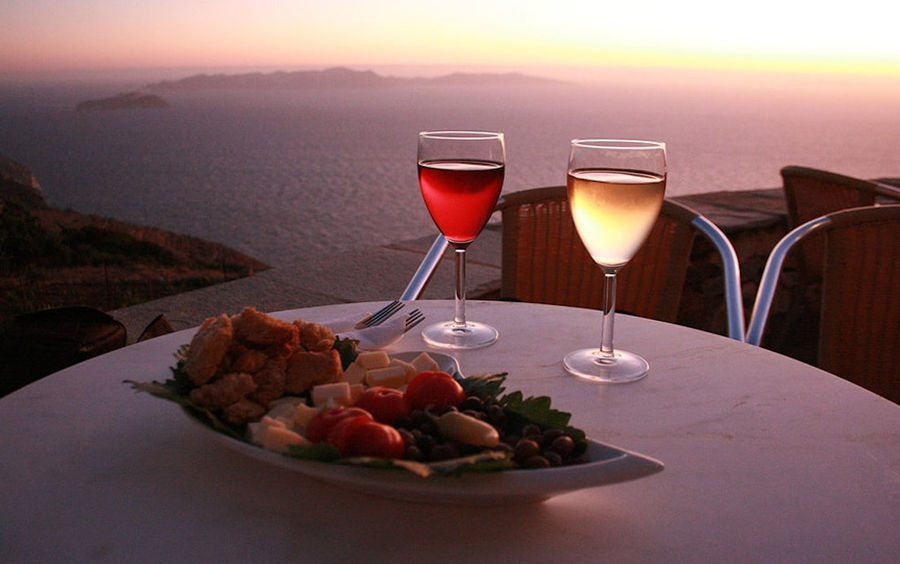 two glasses of wine and plateau with cheese and olives at 'Manalis Winery' background with sea and the sunset